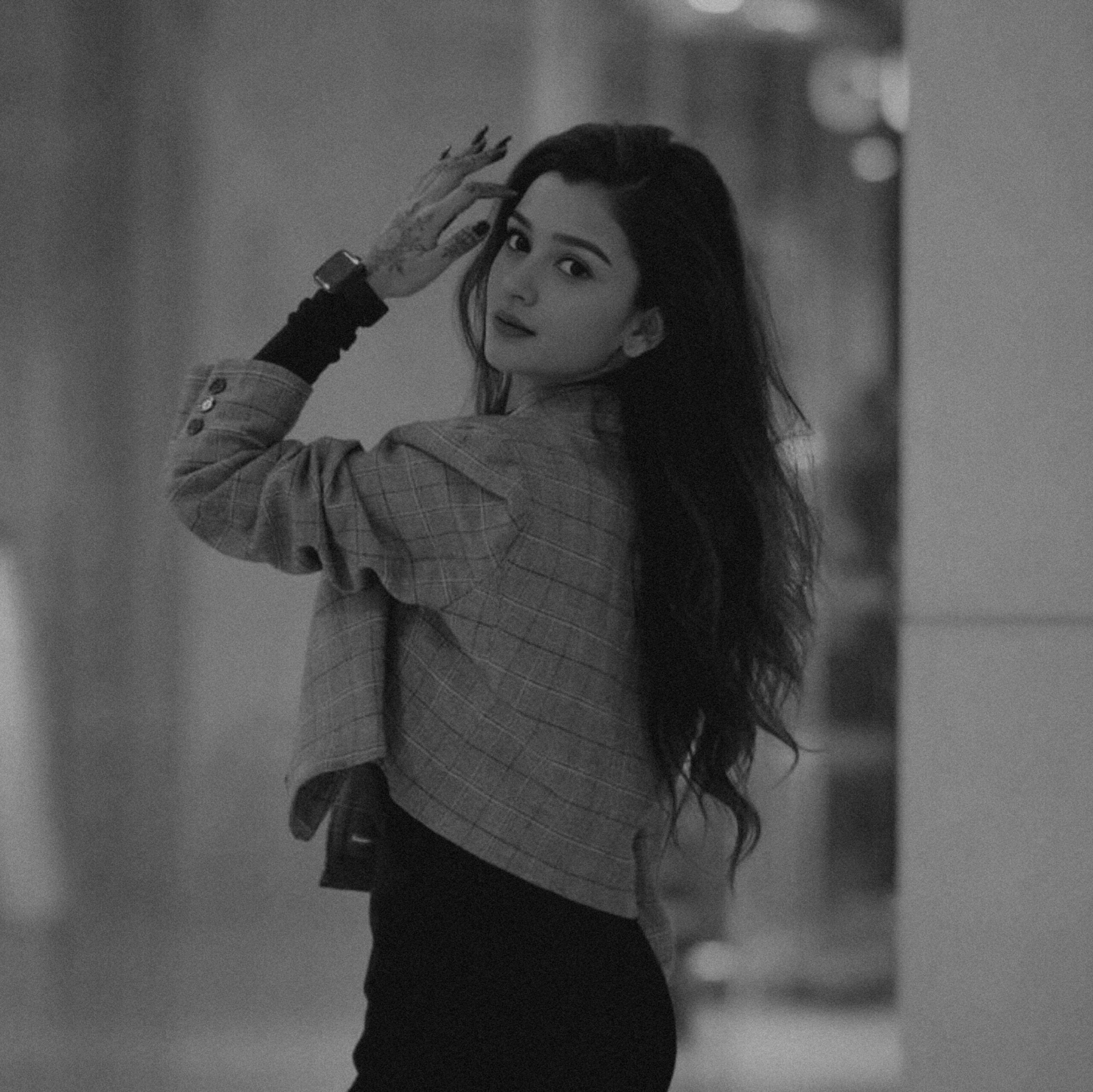Elegant woman in a plaid jacket inside a building, captured in monochrome for a classic feel.